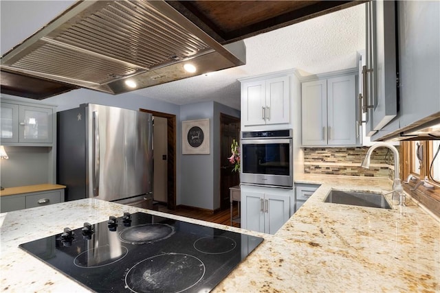 kitchen featuring range hood, light stone counters, a sink, backsplash, and stainless steel appliances