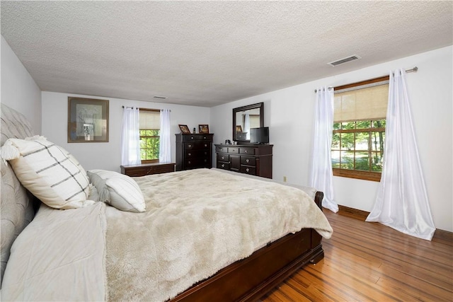 bedroom featuring a textured ceiling, baseboards, wood finished floors, and visible vents