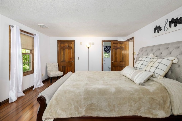 bedroom with a textured ceiling, baseboards, wood finished floors, and visible vents