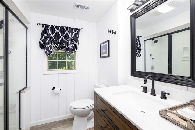 bathroom with vanity, toilet, wood finished floors, visible vents, and a stall shower