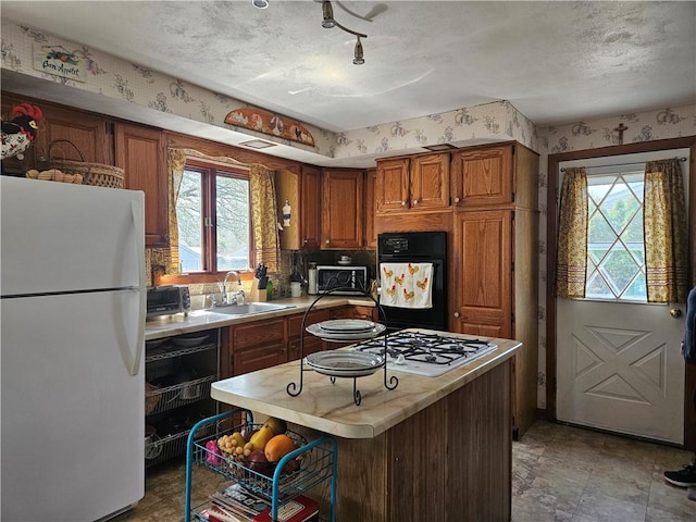 kitchen featuring a sink, wallpapered walls, white appliances, and a wealth of natural light
