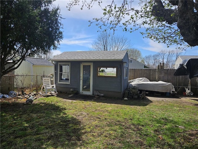 back of property with a fenced backyard, an outbuilding, roof with shingles, and a yard