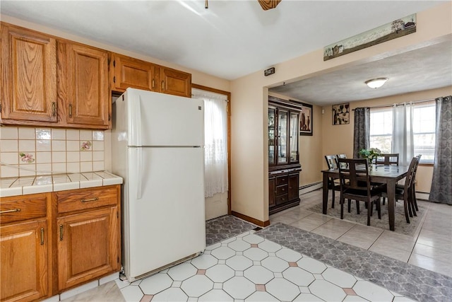 23 Oak Grove Blvd, North Providence, RI 02911 - kitchen with brown cabinets, baseboard heating, tile counters, freestanding refrigerator, and backsplash