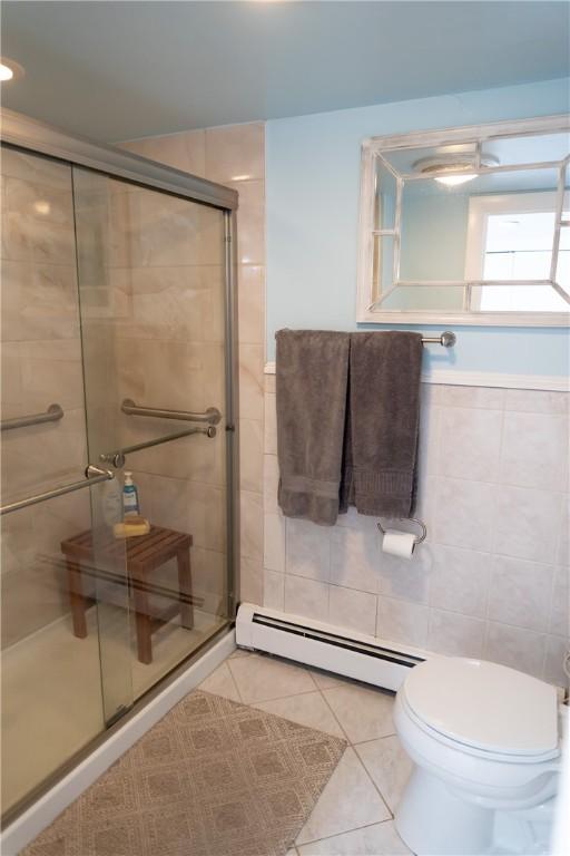 full bath featuring tile patterned flooring, a baseboard heating unit, tile walls, and a shower stall
