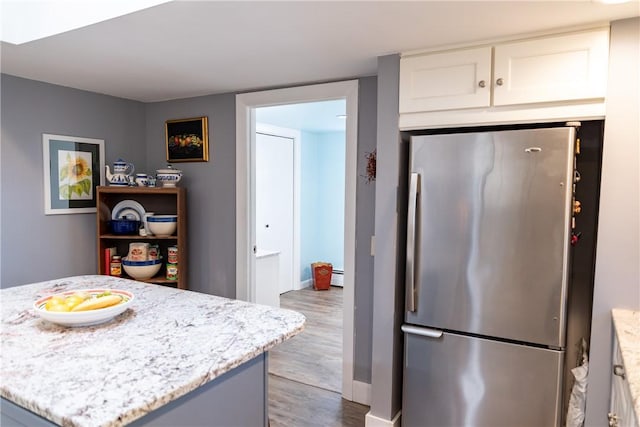 kitchen with freestanding refrigerator, wood finished floors, a kitchen island, light stone countertops, and white cabinetry
