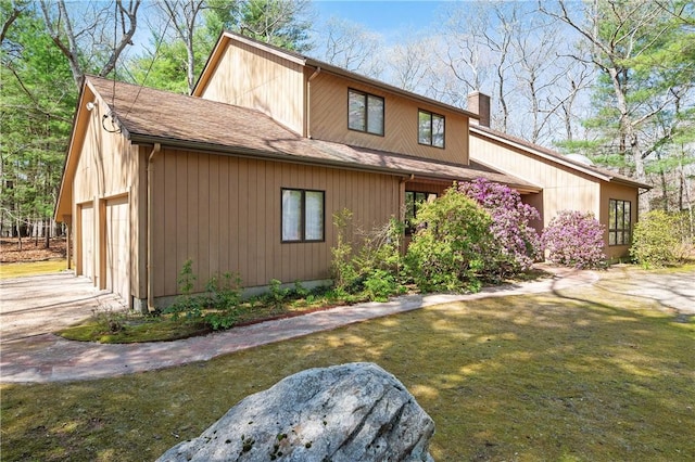 exterior space with a front lawn, a chimney, a shingled roof, concrete driveway, and a detached garage