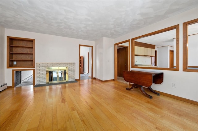 unfurnished living room with a textured ceiling, a brick fireplace, built in shelves, baseboards, and light wood-style floors