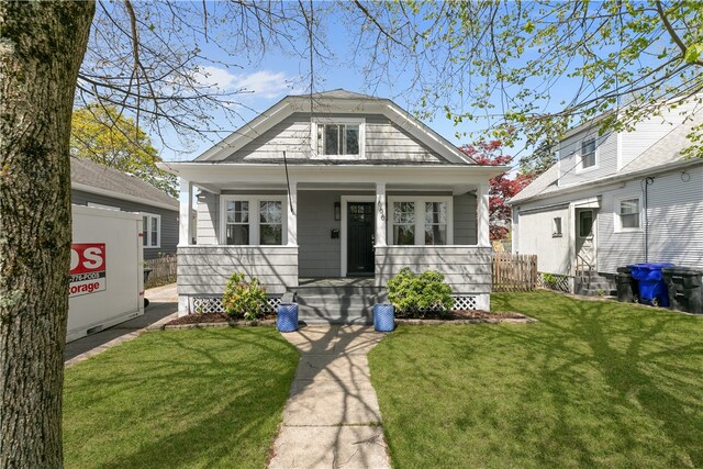 bungalow-style house with covered porch, fence, and a front lawn