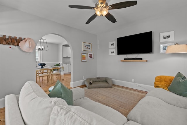 living area featuring baseboards, arched walkways, a ceiling fan, and light wood-style flooring