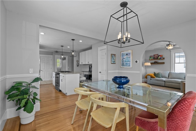 dining room with recessed lighting, arched walkways, ceiling fan with notable chandelier, and light wood-style floors