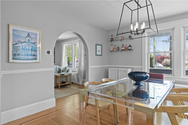 dining room with light wood-style floors, arched walkways, baseboards, and a notable chandelier