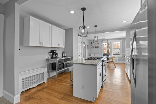 kitchen with white cabinets, light stone countertops, light wood-style floors, stainless steel appliances, and a kitchen island