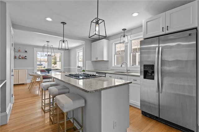kitchen featuring light stone counters, a sink, light wood finished floors, a center island, and stainless steel appliances