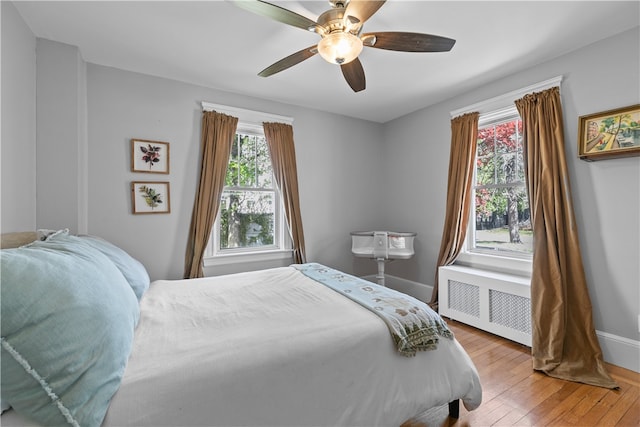 bedroom featuring a ceiling fan, baseboards, radiator heating unit, and light wood finished floors