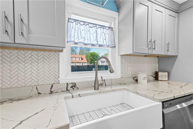 kitchen featuring a sink, backsplash, dishwasher, and light stone countertops