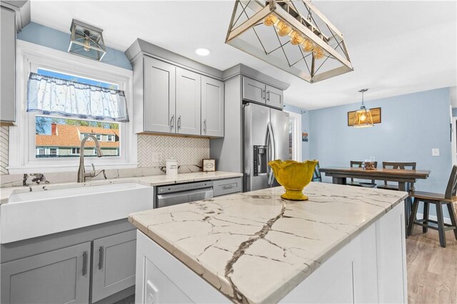 kitchen with gray cabinets, a sink, light stone counters, stainless steel appliances, and light wood-style flooring