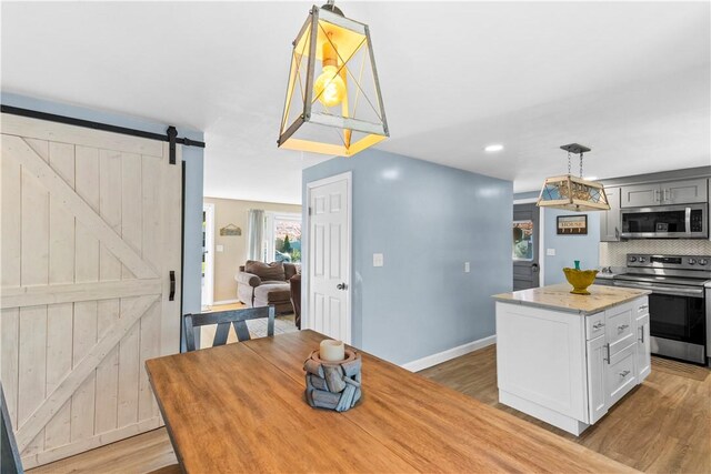 kitchen with baseboards, a barn door, tasteful backsplash, light wood finished floors, and appliances with stainless steel finishes