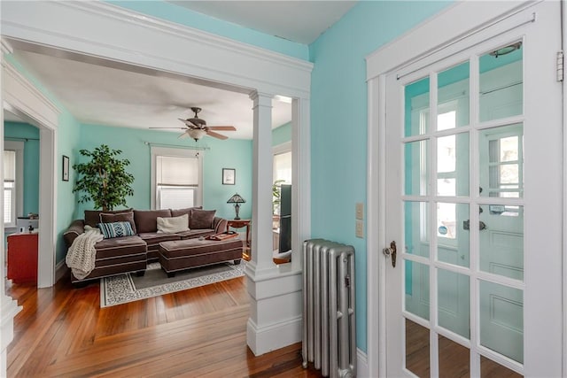 living area featuring radiator heating unit, decorative columns, a ceiling fan, and wood finished floors