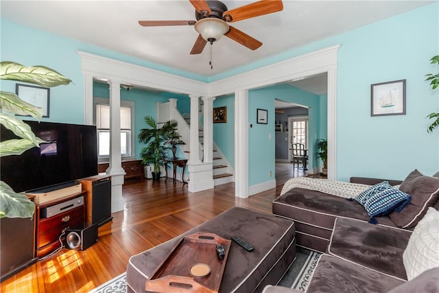 living area with a ceiling fan, decorative columns, wood finished floors, and stairway