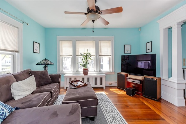 living area with radiator, ceiling fan, ornate columns, and wood finished floors