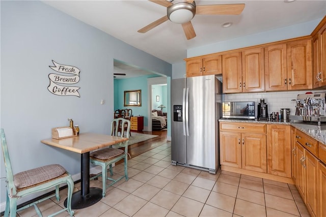 kitchen featuring stone countertops, tasteful backsplash, a ceiling fan, light tile patterned floors, and stainless steel appliances