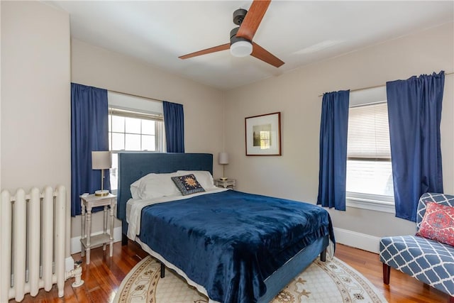 bedroom with wood finished floors, a ceiling fan, baseboards, and radiator heating unit