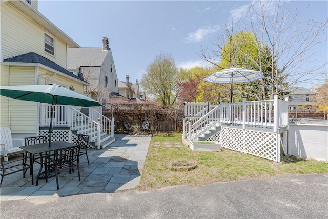view of yard featuring outdoor dining space, a wooden deck, stairway, a fenced backyard, and a patio