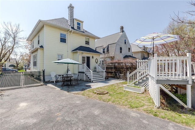 rear view of house with fence, a deck, a patio, a chimney, and a gate