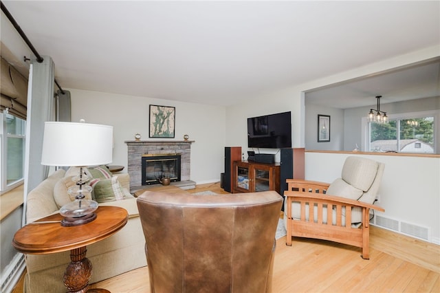 living area with a chandelier, a stone fireplace, light wood-style flooring, baseboards, and visible vents