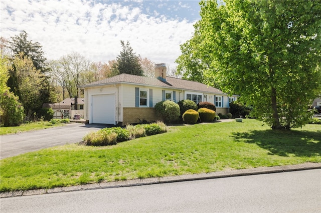 ranch-style home featuring brick siding, a garage, a front yard, a chimney, and driveway
