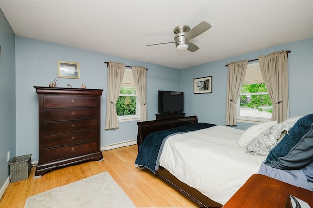bedroom with baseboards, multiple windows, baseboard heating, and wood finished floors