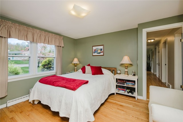 bedroom with light wood-type flooring, baseboards, and a baseboard heating unit