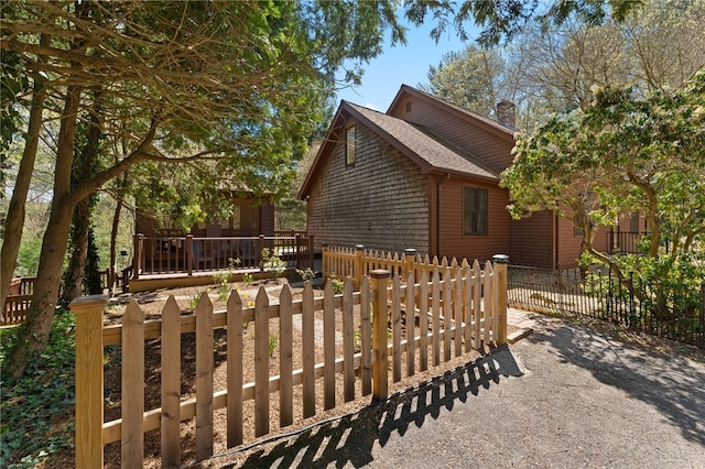 29 Howard Ave, Scituate, RI 02831 - view of side of property with a wooden deck, a fenced front yard, roof with shingles, and a chimney