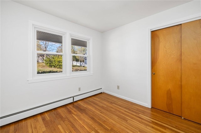 unfurnished bedroom with a closet, baseboards, baseboard heating, and light wood-type flooring