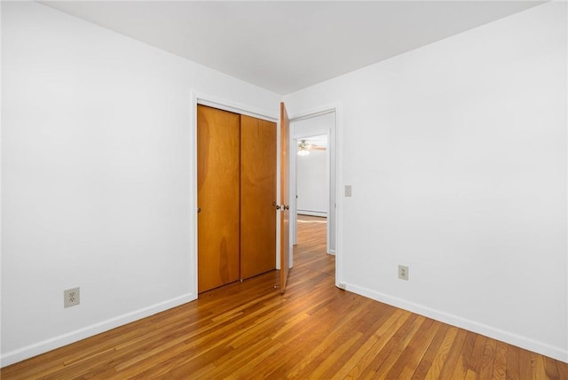 unfurnished bedroom with baseboards, baseboard heating, a closet, and wood finished floors