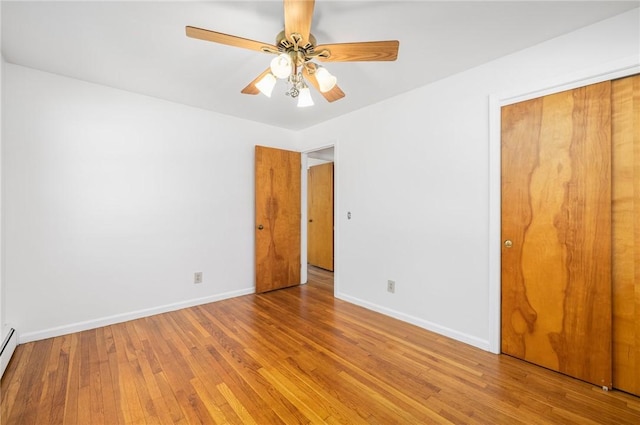 unfurnished bedroom with a ceiling fan, baseboards, wood finished floors, a baseboard radiator, and a closet