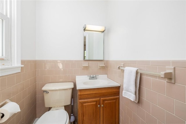 half bathroom with vanity, tile walls, wainscoting, and toilet