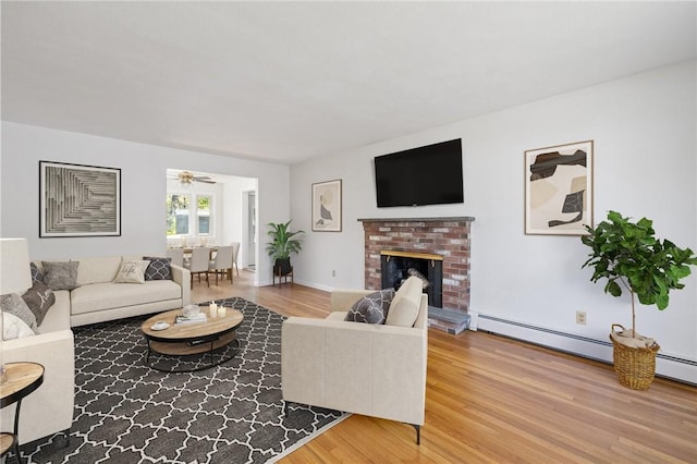 living area featuring ceiling fan, a brick fireplace, and wood finished floors