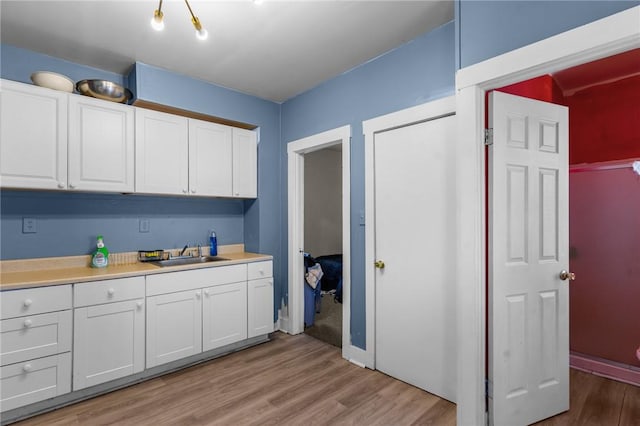 kitchen featuring light countertops, white cabinetry, a sink, and light wood finished floors