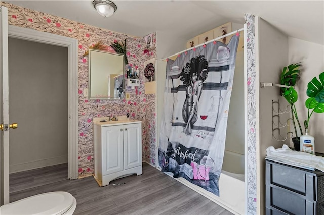 bathroom featuring vanity, shower / bath combination with curtain, baseboards, wallpapered walls, and wood finished floors