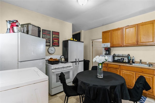 kitchen featuring brown cabinetry, washer / dryer, white appliances, light countertops, and a sink