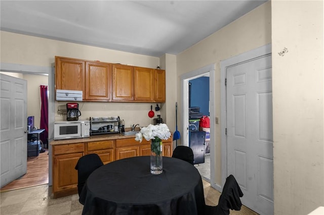 kitchen featuring a sink, light countertops, white microwave, and brown cabinetry