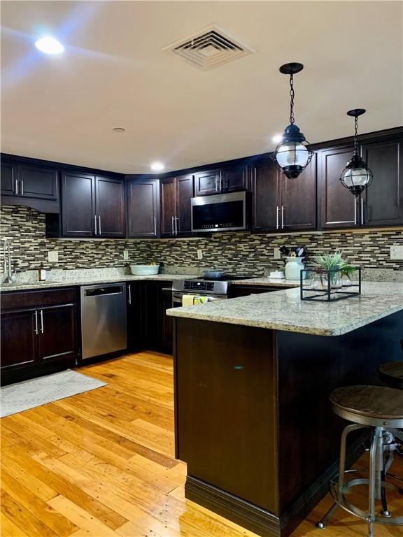 1 Tupperware Dr Unit 233, North Smithfield, RI 02896 - kitchen featuring appliances with stainless steel finishes, a peninsula, light wood-style floors, light stone counters, and backsplash