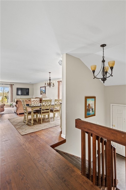 hallway featuring an upstairs landing, lofted ceiling, wood finished floors, and a notable chandelier