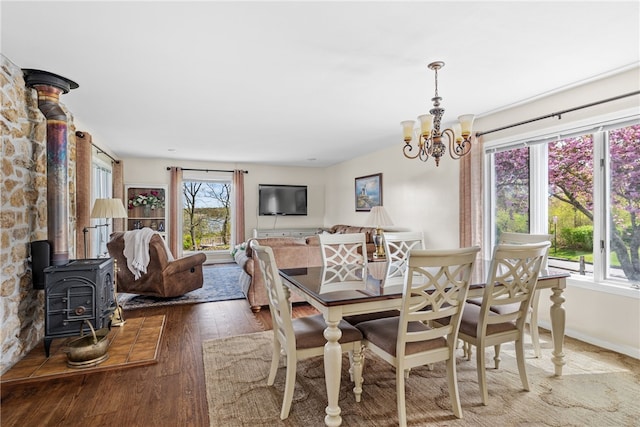 dining room with wood-type flooring, an inviting chandelier, and a wood stove