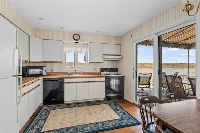 kitchen with wooden counters, a sink, black appliances, under cabinet range hood, and wallpapered walls
