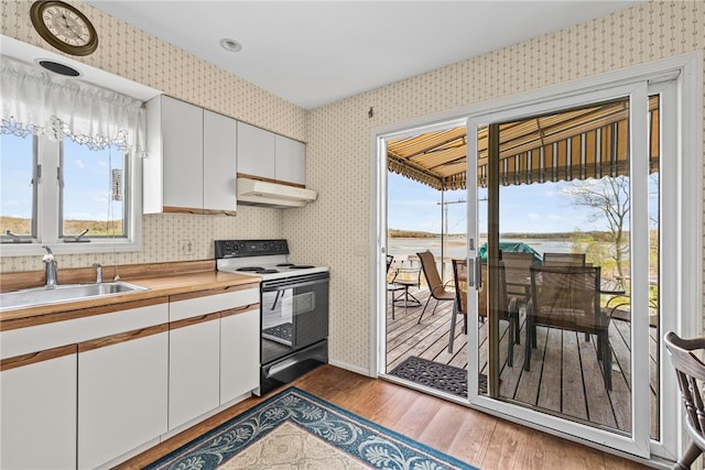 kitchen with a sink, under cabinet range hood, range with electric cooktop, and wallpapered walls