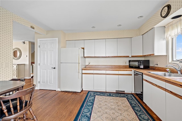 kitchen featuring black microwave, dishwasher, light wood-style flooring, freestanding refrigerator, and wallpapered walls