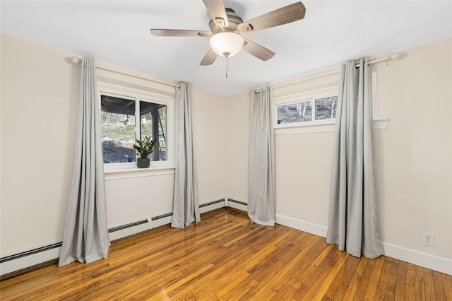 spare room featuring baseboards, plenty of natural light, wood finished floors, and a baseboard radiator
