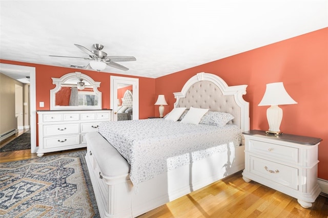 bedroom featuring baseboards, a ceiling fan, light wood finished floors, and a baseboard heating unit